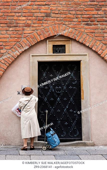 Senior Polish woman returns from shopping and stands at a metal door of a brick townhome, Old Town, Warsaw, Poland, Europe