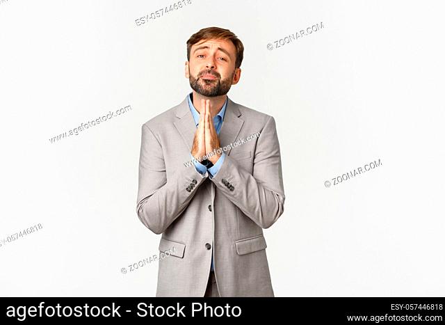 Portrait of bearded male office worker in grey shirt, begging for help or favour, need something, pleading and saying please, standing over white background