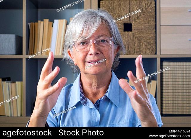 Head shot portrait confident old businesswoman coach wearing glasses looking at camera and talking, mentor speaker holding online lesson, explaining