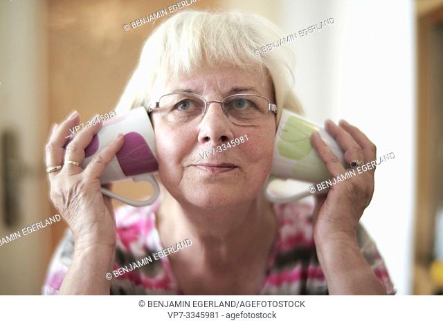 senior woman covering ears with cups at home