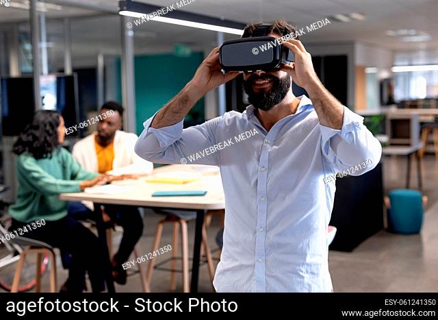 Smiling caucasian businessman wearing virtual reality simulator at modern workplace