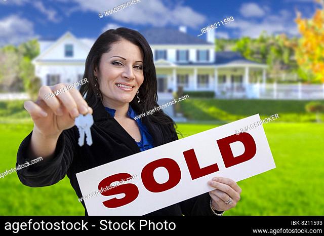 Hispanic woman holding sold sign and keys in front of beautiful house