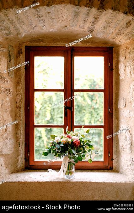 bridal bouquet of white peonies, roses, pink protea, snowberry, branches of eucalypt tree and white ribbons on the window. High quality photo
