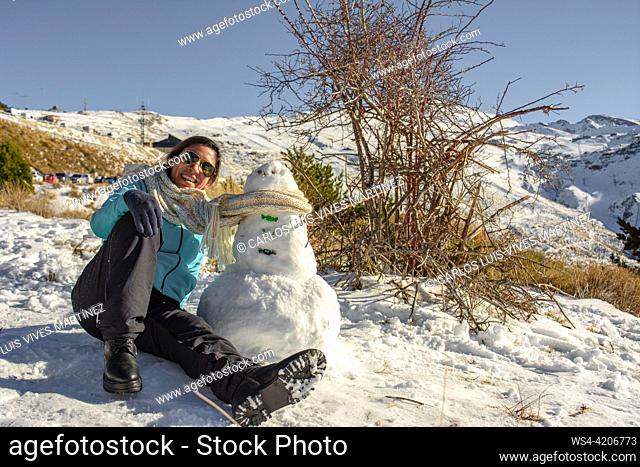latin woman sitting on frozen ground next to snowman,