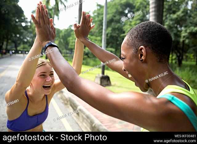 Happy multiracial friends giving high-five at footpath