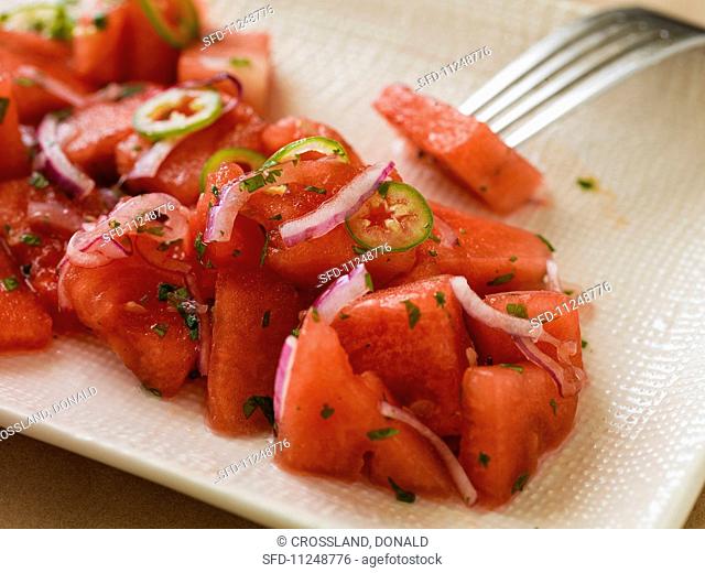 Close-up of watermelon salad with onions and serrano peppers on a rectangular plate with a linen texture