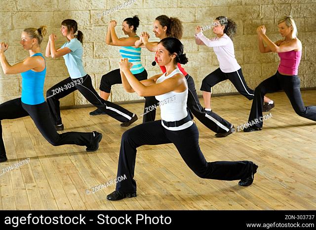 A group of women exercising with fitness instructor in the gym. Focus on the woman in white shirt. Side view