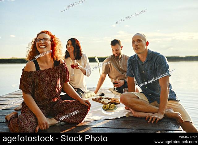 Happy friends having picnic on jetty at a lake at sunset