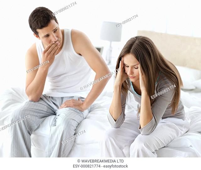Worried man looking at his girlfriend having a headache on the bed at home
