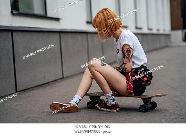 Young woman sitting on carver skateboard on the sidewalk