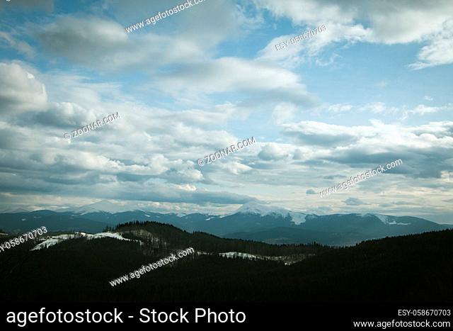 Cloudy sky above snowy forest and mountains