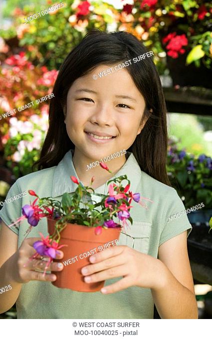 Young girl holding potted flowers in plant nursery portrait