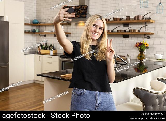 Young excited woman taking a selfie in her new apartment kitchen