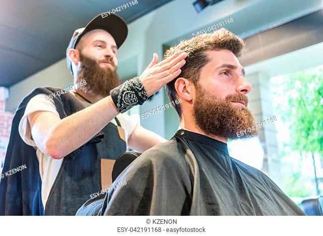 Low-angle view of a handsome bearded young man, ready for a trendy haircut done by an experienced hairstylist in a cool beauty salon for men