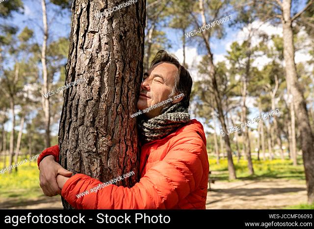 Man with eyes closed hugging tree trunk in forest