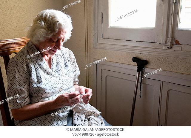 Portrait of elderly woman crochetting at home, by the window