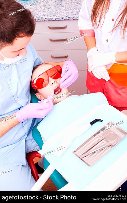 Teenage patient lies in special glasses for protection against laser beams while the dentist works with dental curing light. Teeth care concept