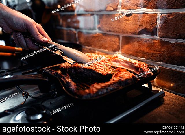 Hand turns steak with tongs during preparation on the grill pan with seasonings. High quality photo