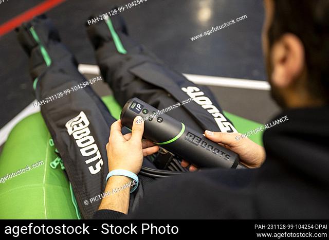 28 November 2023, Bavaria, Munich: A trade fair visitor tries out a pair of multi-chamber regeneration pants at the Reboots stand during the ISPO sporting goods...
