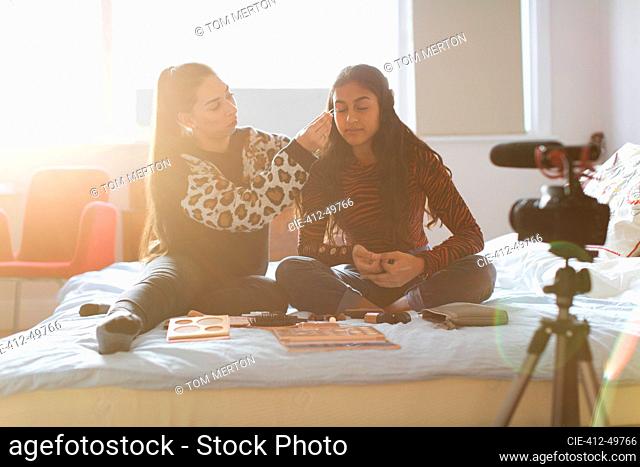Teenage girls vlogging, demonstrating makeup application in sunny bedroom