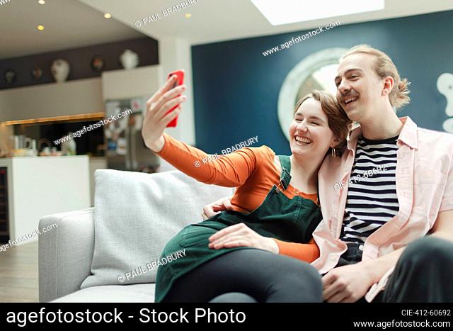 Happy young couple taking selfie on living room sofa