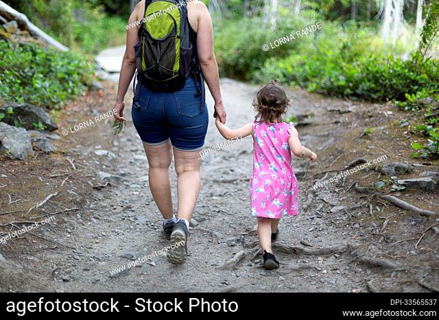 Mother and young daughter hold hands and walk down a trail on a hike together in Smuggler Cove Marine Provincial Park along the Sunshine Coast of BC