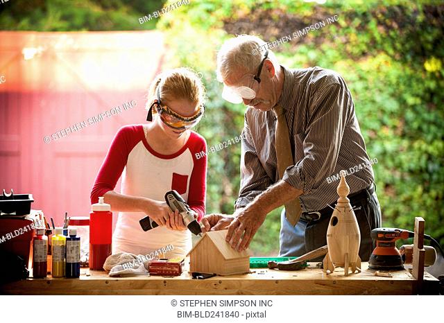 Grandfather helping granddaughter build birdhouse in garage