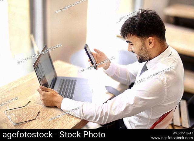 Businessman comparing differing appearance of internet website on laptop and on smartphone