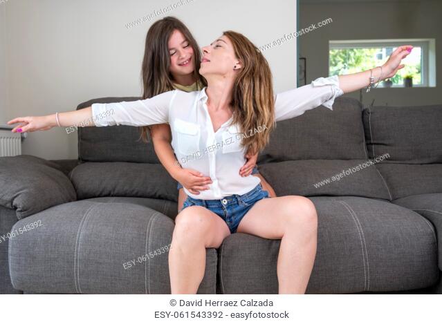 Portrait of playful and excited little girl holding her mother hands while pretending to fly for fun at home. Happy caucasian mother bonding and relaxing with...