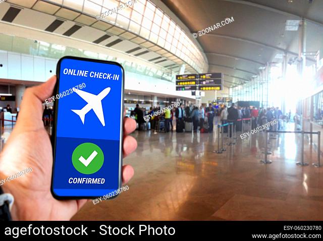 The hand of a man holding a mobile phone with the online check in confirmation message on the screen inside an airport. Travel and technology concept