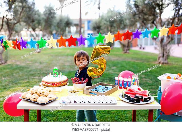 Little boy with golden balloon behind laid birthday table