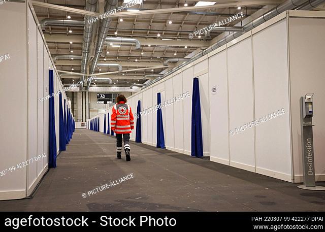 07 March 2022, Hamburg: A Red Cross volunteer walks through rows of emergency accommodation for refugees in Hamburg's exhibition halls