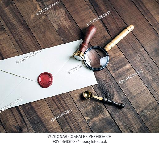 Vintage stationery mockup. Photo of blank envelope, sealing wax, stamp, magnifier and spoon on wood background. Template for placing your design