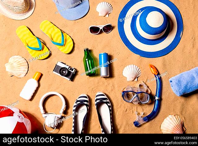 Summer vacation composition with a pair of yellow flip flop sandals, hat, sunglasses, goggles, sunscreen and other stuff on a beach