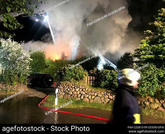 10 August 2022, Schleswig-Holstein, Kampen: Firefighters extinguish a burning house. A fire in a thatched house in Kampen on the island of Sylt triggered a...