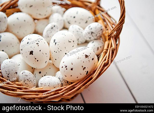 Basket of chicken and quail white dotted Easter eggs in brown wicker basket. Placed on white wooden table