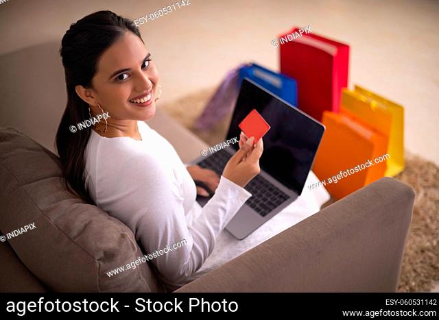 Beautiful Indian girl looking at camera during online shopping through laptop using debit card