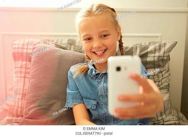 Girl sitting on bed using smartphone to take selfie smiling