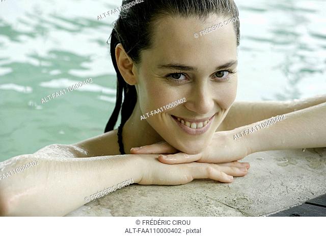 Woman in swimming pool at edge resting head on arms