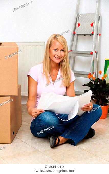 young woman happily sitting on the floor of her new flat beside moving box