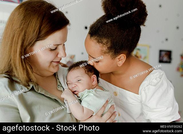 Happy mother with daughter kissing baby girl at home