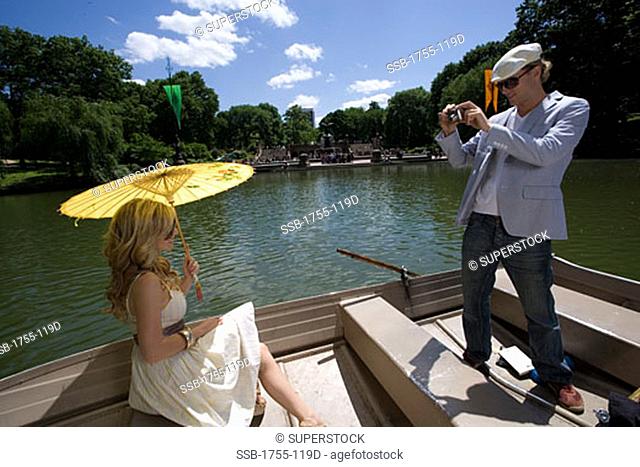 Young man taking a picture of a young woman sitting in a boat, Central Park, Manhattan, New York City, New York, USA