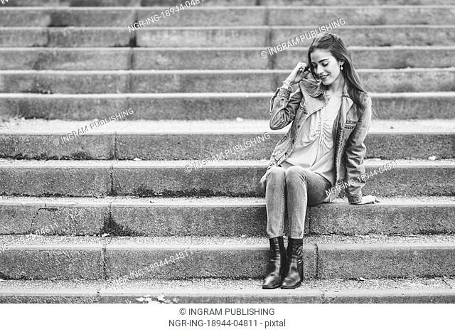 Young woman with nice hair wearing casual clothes in urban background. Happy girl with wavy hairstyle sitting in urban stairs