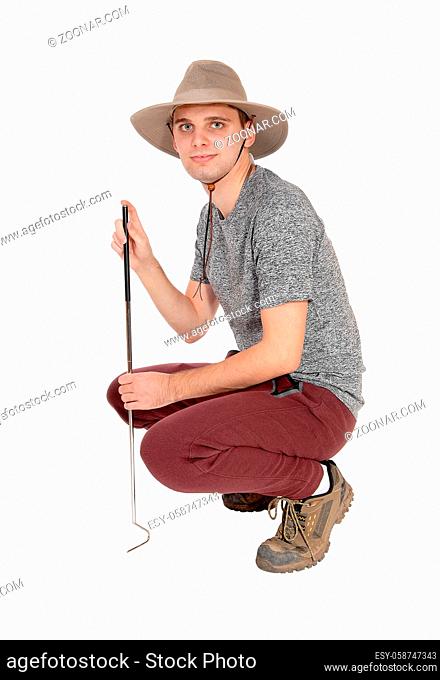 A slim young man in a gray sweater with a safari hat and a tool to catch some snags crouching on the floor, isolated for white background