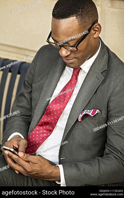 Black businessman using cell phone on bench