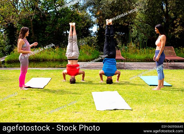 Full length of women looking at men practicing handstand in park on sunny day