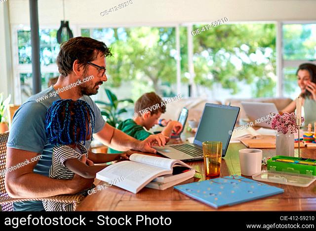 Father working from home at laptop with daughter on lap