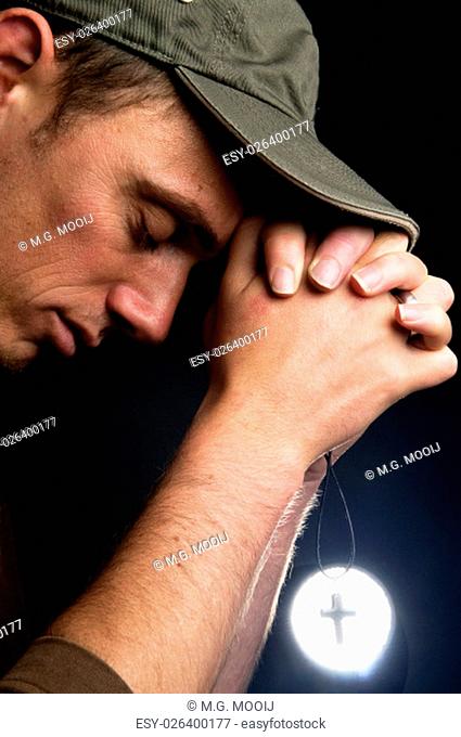 Praying man holding a cross in front of a bright light