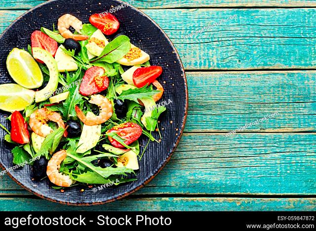 Salad with shrimps, strawberries, avocado and herbs.Seafood salad on rustic wooden background.Copy space, space for text