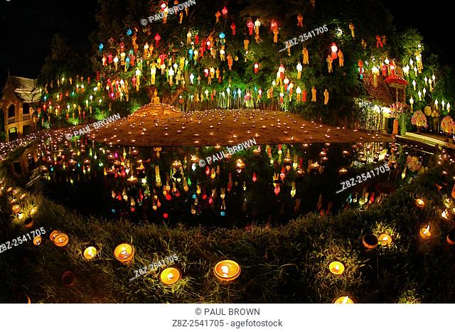 Lanterns and candles reflected in a pool with a Buddha stature for the Loy Krathong Festival at Wat Phan Tao Temple in Chiang Mai, Thailand